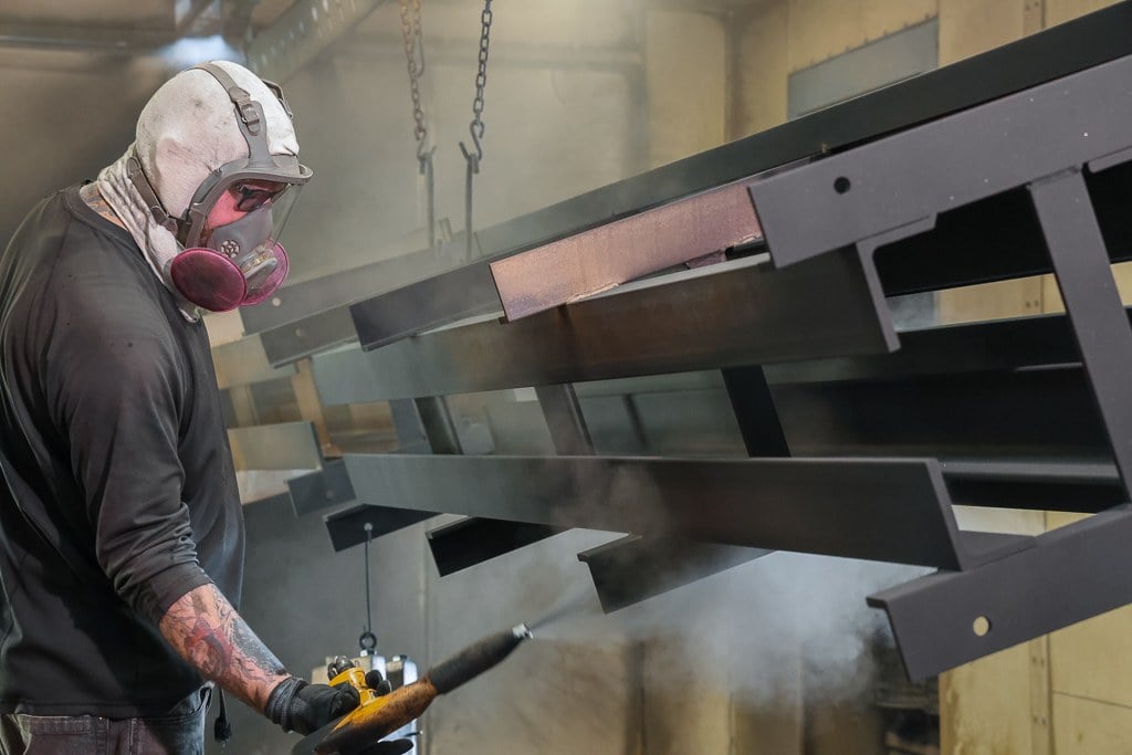 Technician in a respirator spraying powder coat on steel parts