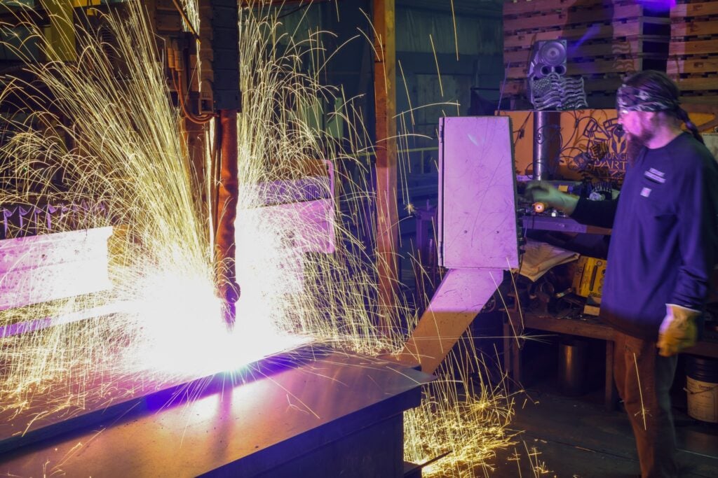 Operator watching a CNC plasma cutter throw sparks across a steel plate