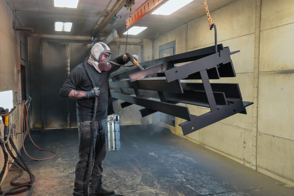Operator spraying powder coat onto steel parts hanging in the powder booth