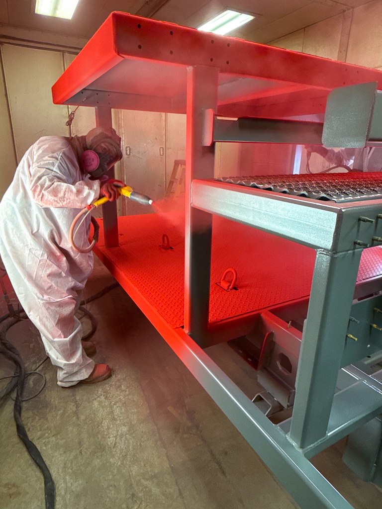 Red Oak team member in a protective suit powder coating a steel frame in the spray booth