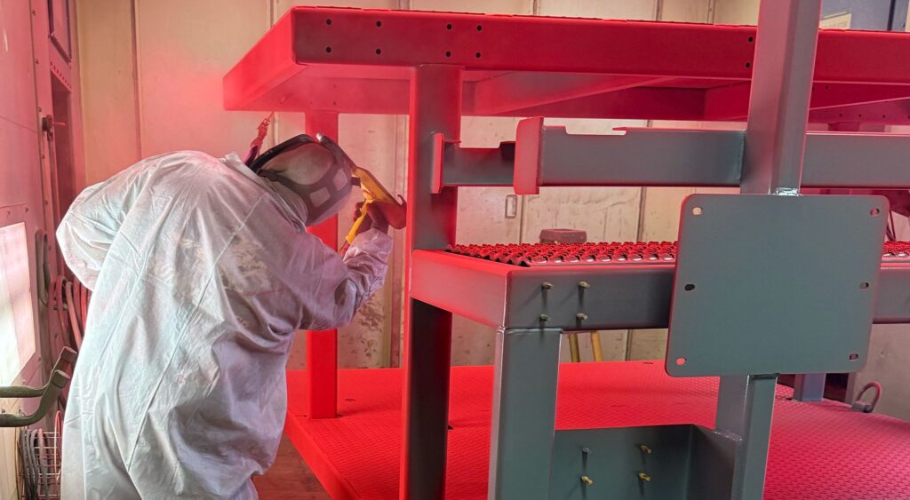 Operator powder coating a welded steel assembly in the paint booth